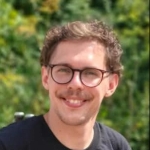 l&auml;chelnder junger Mann mit braunen Haaren und Brille